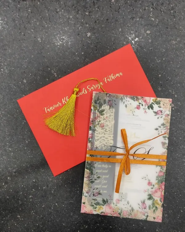 A complete view of a vibrant and elegant invitation suite. It includes a floral vellum wrap tied with a ribbon, a main invitation card, and a bold red envelope with the couple's names in gold foil.