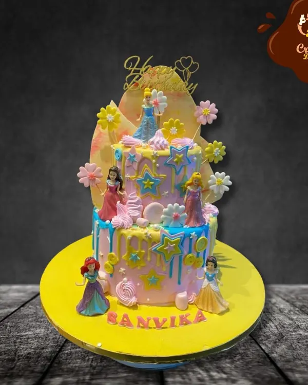 A dreamy two-tier cake featuring several Disney princesses. The pastel colors, star decorations, and drip effect create a magical backdrop for figures of Cinderella, Ariel, and others.