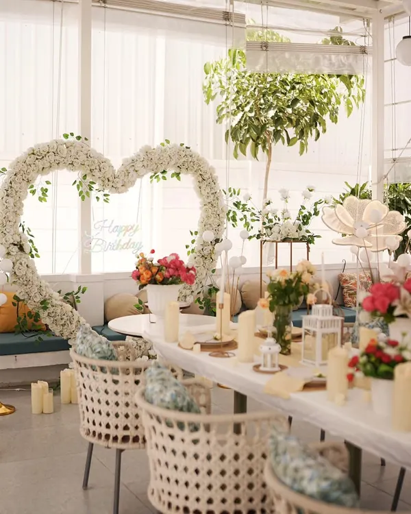 A bright and beautiful daytime celebration. The large white floral heart, fresh flowers, and elegant table setting create a perfect scene for a birthday lunch or anniversary brunch.
