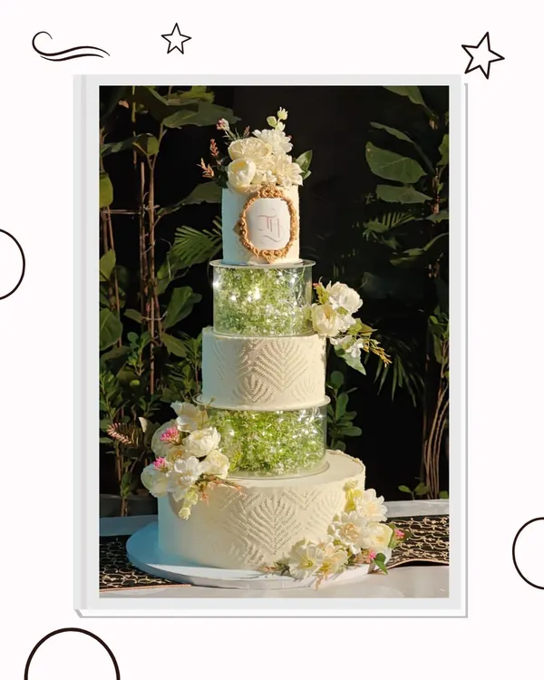 This multi-tiered wedding cake is a true showstopper, designed to be the centerpiece of a grand celebration. It features elegant textures, separator tiers filled with delicate baby's breath, and is adorned with handcrafted sugar flowers and a custom monogram.