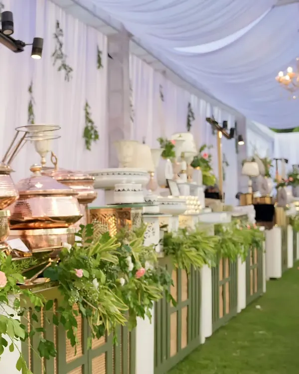 A preview of our elegant outdoor wedding catering setup. This expansive buffet features our signature hammered copper serving dishes, lush green and pink floral arrangements, and is set against a beautifully draped marquee, creating a sophisticated atmosphere for a day wedding.