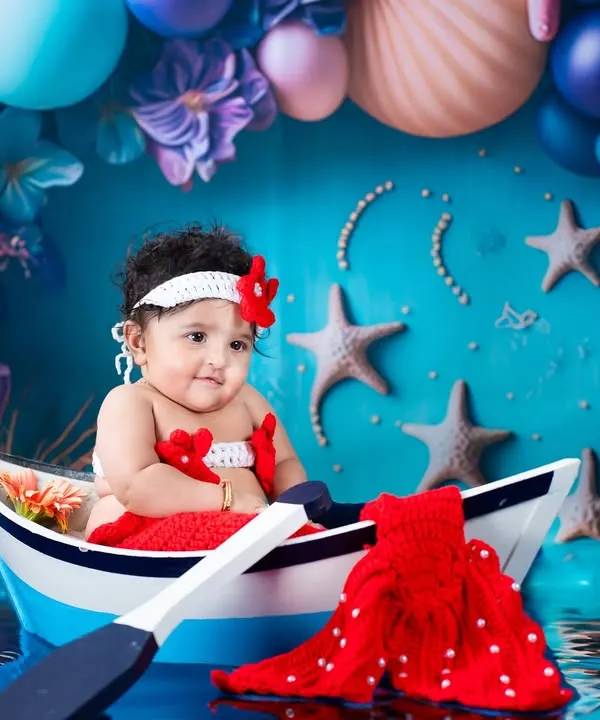 Our little mermaid is ready for an ocean adventure! This vibrant, underwater-themed setup features a custom boat, a knitted mermaid tail, and a sea of colorful balloons and starfish.