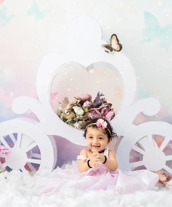 A true fairytale moment. This little princess is all smiles in her magical butterfly-themed carriage, surrounded by flowers and soft clouds.