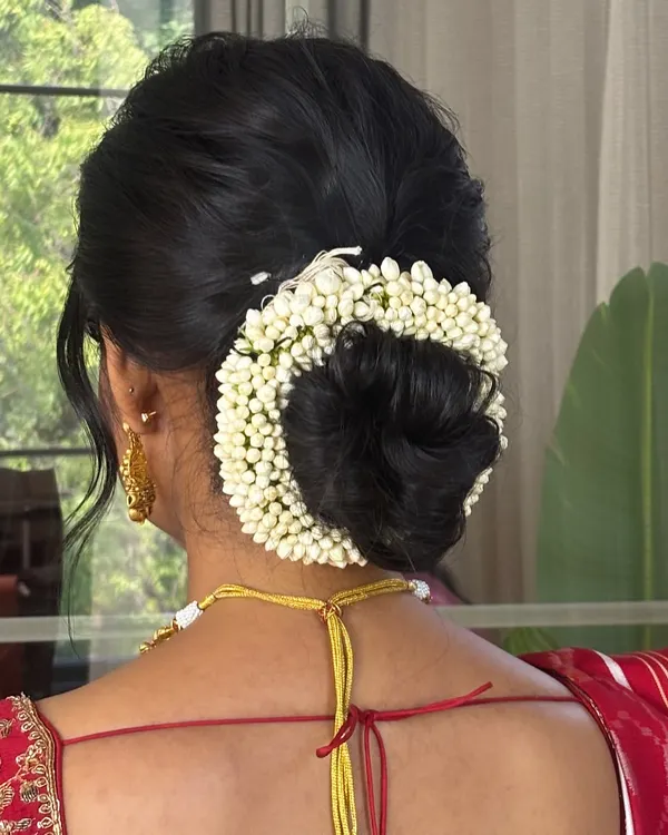 A closer look at this flawless traditional bridal bun. The hair is smoothly swept back and secured into a perfect low bun, encircled by a thick, fresh jasmine gajra. This is a classic South Indian bridal hairstyle that is always in vogue.