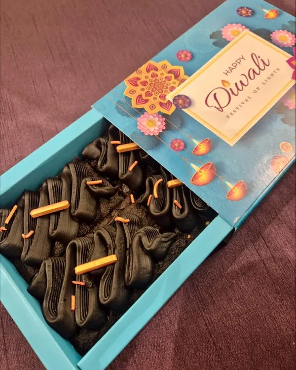 A box of my signature fudgy brownies, decorated with dark chocolate piping and sprinkles, presented in a beautiful "Happy Diwali" gift box. A perfect festive treat.