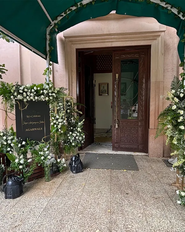 We create elegant welcome areas that set a sophisticated tone. This setup features a classic black and gold sign surrounded by lush arrangements of white roses and greenery.