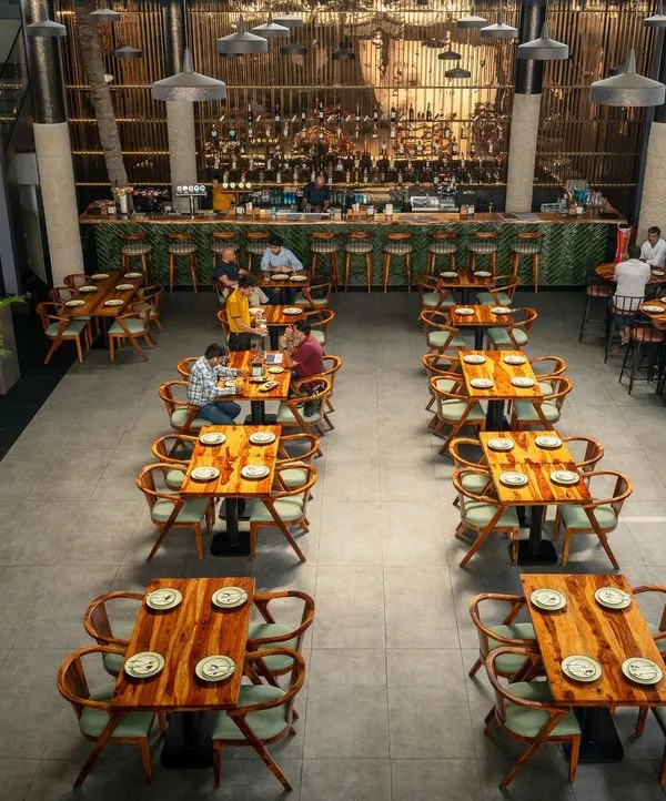 An overhead view of the main dining hall at Pincode 24. This perspective shows the flexible seating arrangement with a mix of low and high tables, the expansive concrete-texture tile flooring, and the impressive scale of the double-height space leading to the bar.