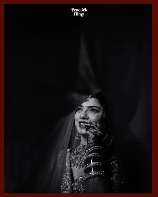 Behind the veil, a universe of emotions. This black and white portrait uses dramatic lighting to capture the bride's joyful, upward glance and the delicate details of her attire.
