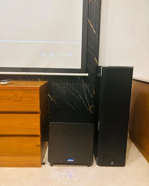 A complete home theater system ready for action, featuring floor-standing speakers, a powerful subwoofer, and a large projector screen. This is how you get movie nights that feel just like the cinema.
