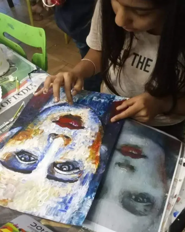 A young student deeply focused on her portrait painting, using a reference photo to learn about texture and color application with a palette knife.