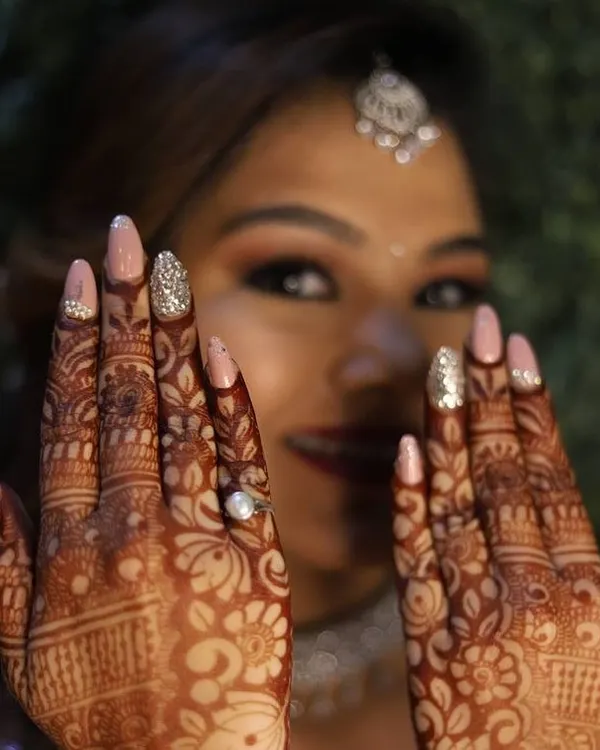 A happy bride showing off her custom wedding nails. This set features a soft pink base with a sparkling silver glitter accent nail, designed to complement her intricate henna and wedding attire.