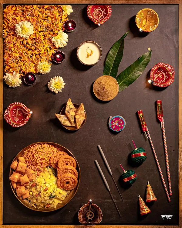 A festive flatlay showcasing the essentials of a Maharashtrian Diwali. This frame includes 'faral' like chakli and shankarpali, diyas, flowers, and firecrackers, artistically arranged to capture the complete essence of the celebration.