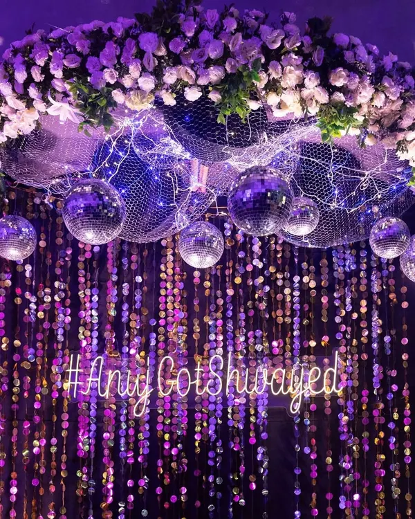 A custom neon sign with the couple's hashtag, '#AnujGotShwayed', served as a cool, modern photo backdrop against a wall of shimmering sequins and disco balls.