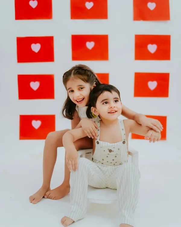 A sweet moment between two sisters during their studio photoshoot. The simple backdrop of red hearts makes their connection the main focus.