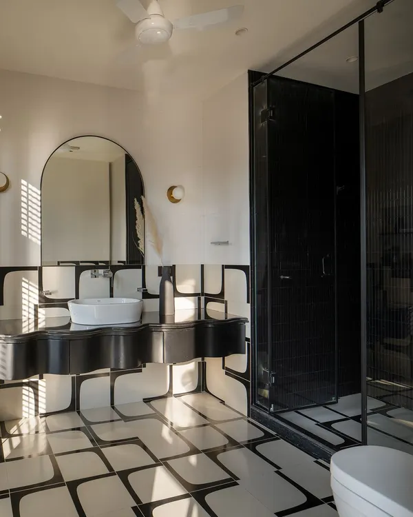 A bold monochrome bathroom with custom-designed tile patterns and an undulating black vanity. The sculpted countertop adds an artistic touch, while soft curves balance the geometry.