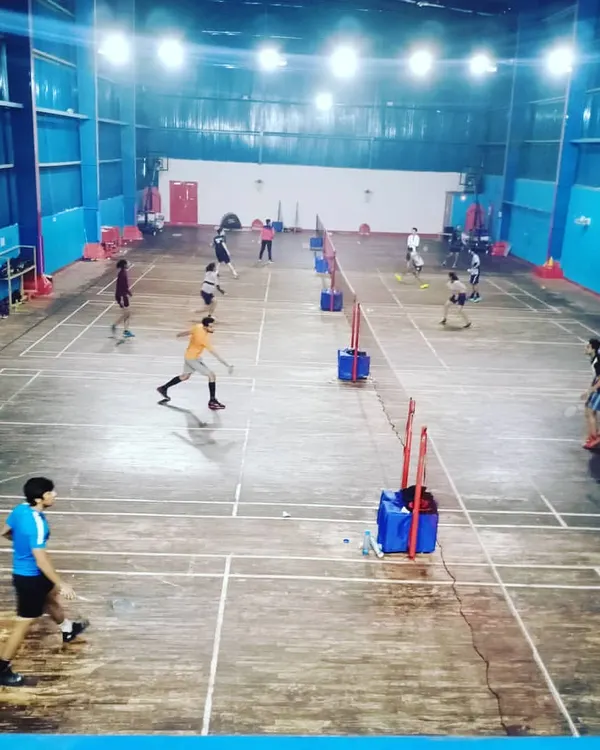 A high-angle view of our bustling multi-court badminton hall in Indirapuram. This shot captures the energetic atmosphere during a peak practice session on our polished wooden courts, with multiple games happening simultaneously under bright, professional-grade lighting.