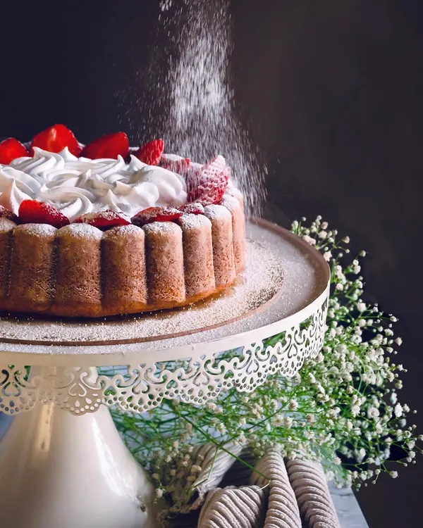 A stunning shot of a strawberry-topped cake being dusted with powdered sugar, capturing a moment of kitchen magic.
