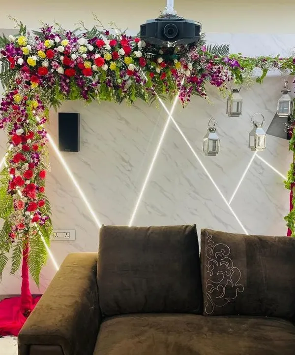 An L-shaped floral arch designed to fit perfectly in a living room for a small function. This arrangement uses a mix of colorful flowers and ferns to create a beautiful frame over the main seating area without taking up too much space.