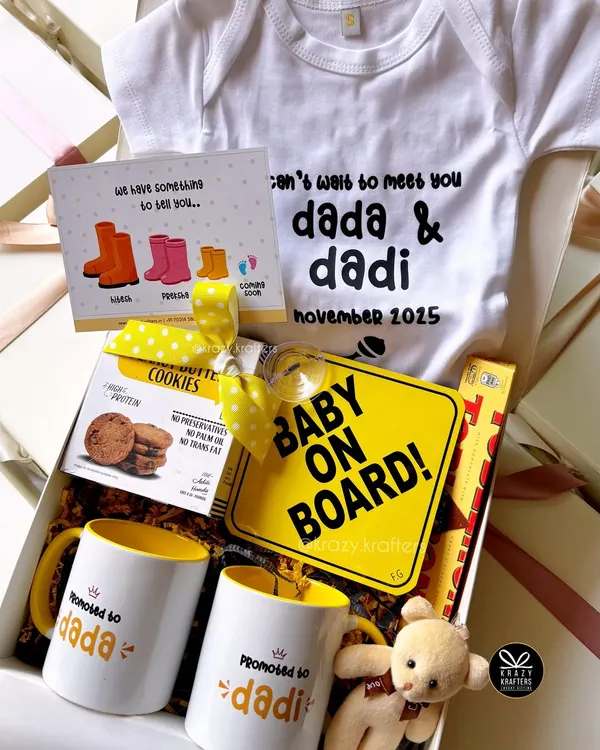 A complete pregnancy reveal hamper for the grandparents-to-be. This box includes 'Promoted to Dada & Dadi' mugs, a custom onesie, a 'Baby on Board' sign, and other sweet treats to make the announcement extra special.