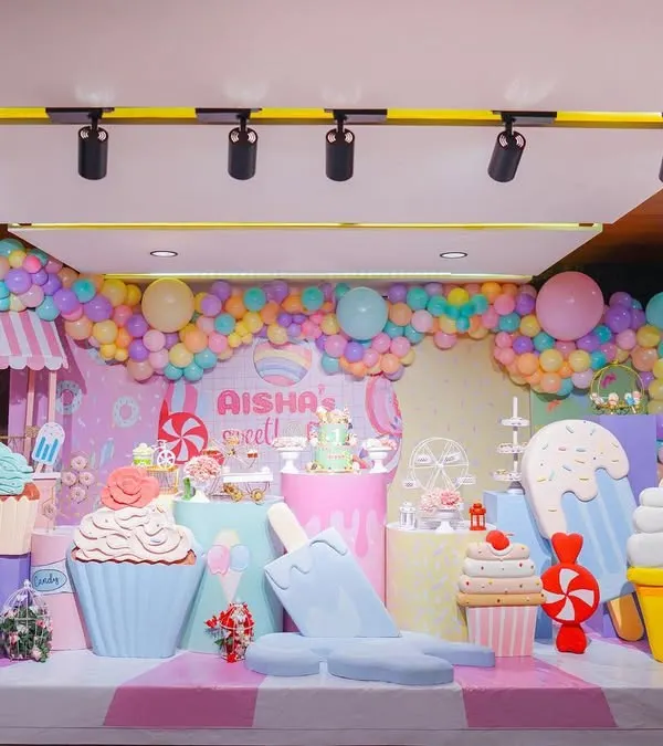Welcome to Aisha's Sweet One! This Candyland stage is a sugar-coated dream, filled with giant cupcakes, ice cream cones, macarons, and a pastel balloon garland. It's a feast for the eyes!
