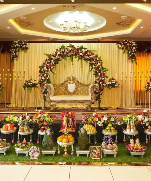A complete setup for a Baby Shower at Chandapura. This shows the main stage with a floral arch and ornate sofa, along with a full display of artfully arranged Seer Thattu plates in the foreground.
