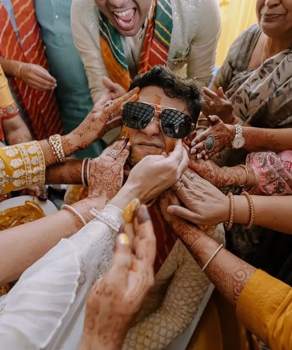 The perfect candid Haldi moment. The groom is surrounded by family, all joyfully applying turmeric paste. It's chaotic, fun, and full of love.