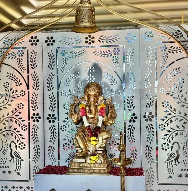 A divine beginning with a beautiful Ganpati idol set against an intricate white jali backdrop, adorned with temple bells, symbolizing blessings and auspiciousness.