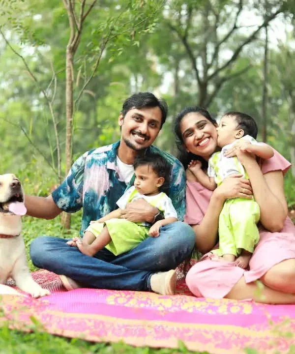 A beautiful family portrait in an orchard, featuring a happy couple with their twin babies and their first child, Snowy the Labrador, by their side.