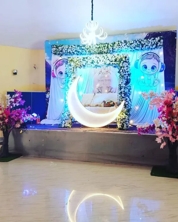 A cute, cartoon-themed baby shower decoration. The stage features a blue and white backdrop, a small moon prop, and character cutouts, perfect for a playful celebration.