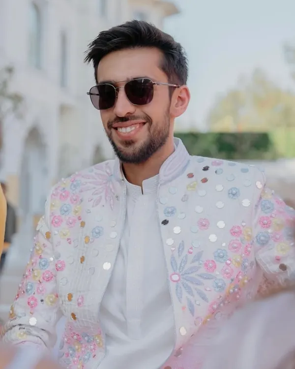 A closer look at the groom's jacket from our coordinated family ensemble. The white base is brought to life with multi-colored floral embroidery and mirror work, perfectly matching the bride's outfit for a cohesive and stylish look.