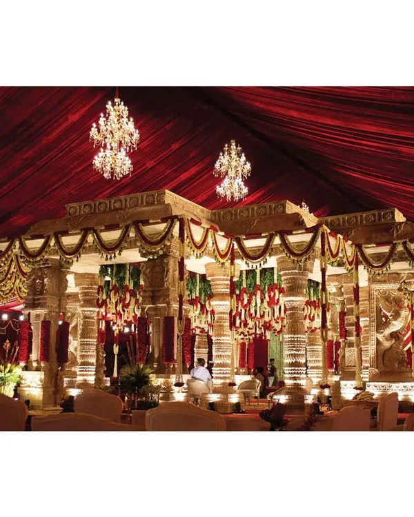 This is a wide view of the Hampi-inspired temple mandap my team and I constructed. The design features intricately carved pillars, a rich red fabric ceiling, and sparkling chandeliers to create a sacred space that feels both grand and deeply traditional.