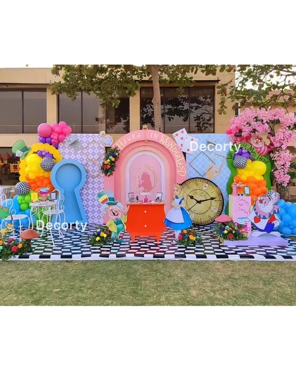 A sprawling, vibrant "Alice in Wonderland" setup in a garden. This whimsical scene features multiple photo ops, including a keyhole cutout, a Mad Hatter tea party, and character props.