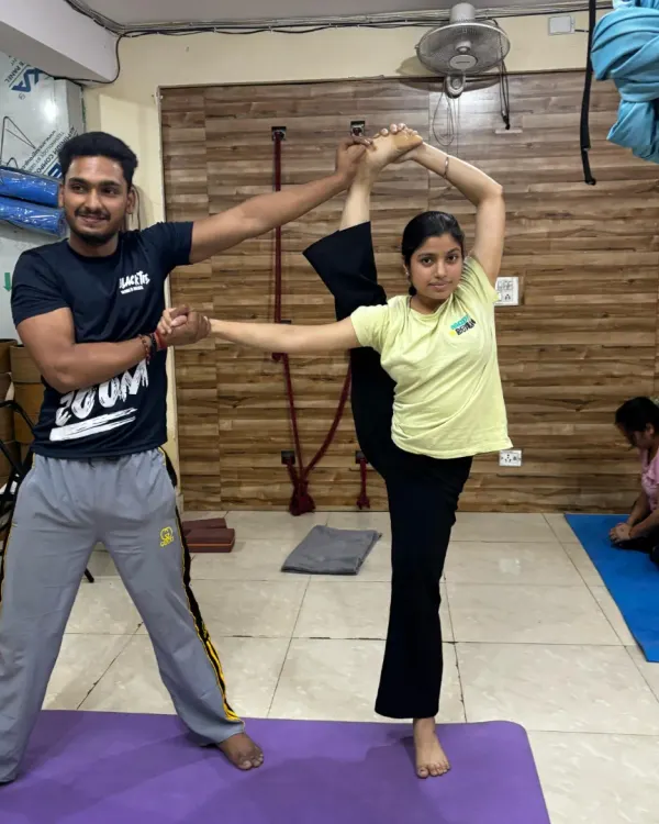 An instructor provides support in a standing split variation, helping the student achieve greater height and maintain balance. This hands-on technique ensures stability in advanced balancing poses.