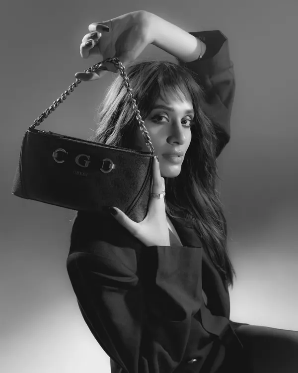 A classic black and white portrait for an accessories campaign. The high-contrast lighting and the model's pose, framing her face with the bag, create a timeless and chic image.