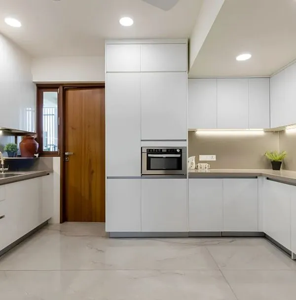 This all-white U-shaped kitchen is a study in modern minimalism. The handleless cabinets, integrated microwave, and under-cabinet lighting create a seamless and brightly lit workspace.