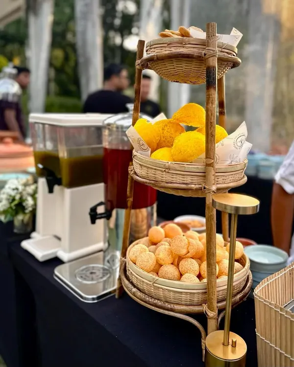 A beautiful bamboo stand presents the elements for a classic pani puri station. It holds crispy puris and large glass dispensers for sweet and spicy flavored waters, ready for guests to create their own chaat.