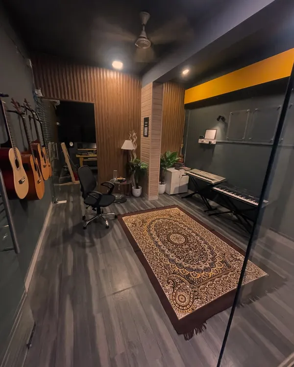 A wide view of our main studio room at HSR Layout. It showcases the blend of warm wood paneling, comfortable seating, and professional equipment like the keyboard and wall-mounted guitars.