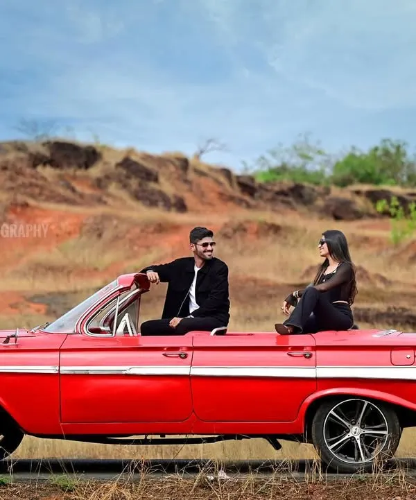 A cinematic pre-wedding portrait using a vintage red convertible as a prop. This shoot captures a cool, editorial vibe against a rustic, open-road backdrop, perfect for couples wanting a unique and stylish session.