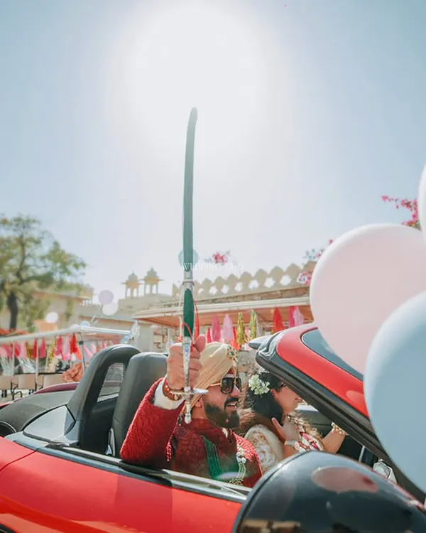 A grand entrance for the groom in a fiery red Porsche convertible, holding a traditional sword. This is how you make a statement and kick off the baraat with style and energy.
