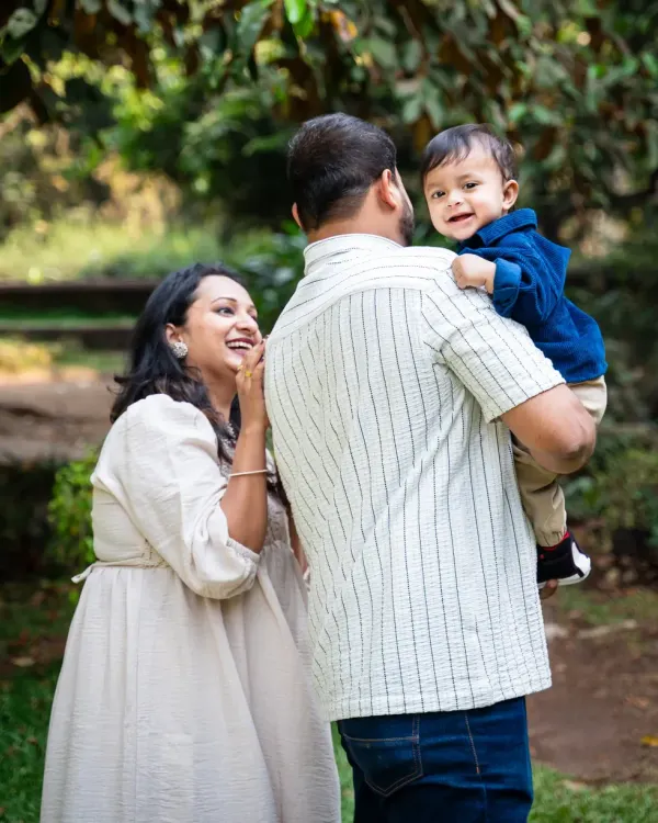 A candid family moment outdoors, with the baby looking back over his father's shoulder with a big smile.