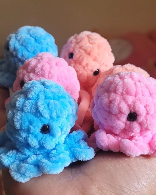 A handful of my adorable, fluffy octopus keychains. This close-up shot shows the detail in their little eyes and the soft texture of the velvet yarn in shades of blue, pink, and peach. They are a customer favorite at my market stalls.