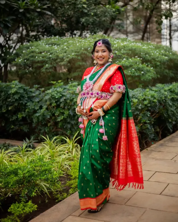 A full-length portrait of the mom-to-be at her outdoor Dohale Jevan, looking radiant in a traditional green and red Paithani saree.