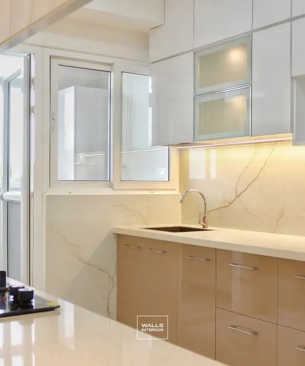 This kitchen showcases an elegant and bright design with high-gloss beige lower cabinets and white upper cabinets. The space feels open and airy, with a utility balcony accessible directly from the kitchen.
