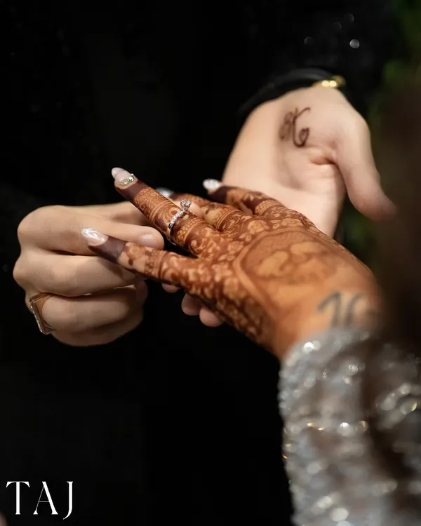 A close-up of the ring exchange, a pivotal moment in any engagement ceremony. I focus on details like the henna and the couple's initial tattoo.