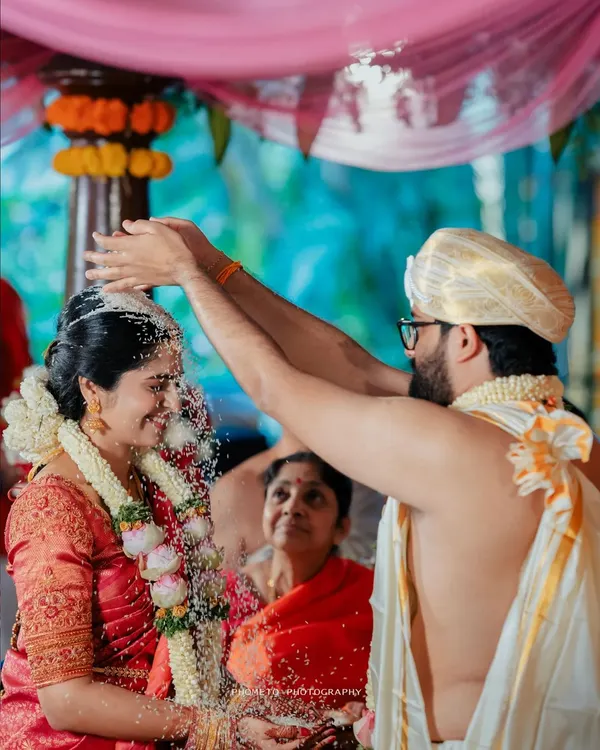A sacred moment as the groom showers the bride with rice, a significant ritual in many South Indian weddings, captured with a focus on her joyful expression.