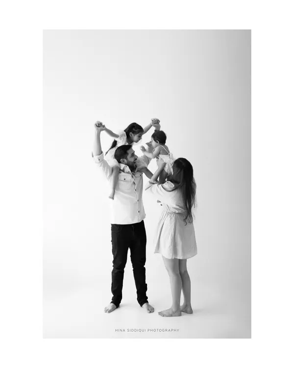 The world from up high. This joyful family portrait captures a playful moment with both children lifted onto their parents' shoulders. It’s a beautiful representation of family support and fun.