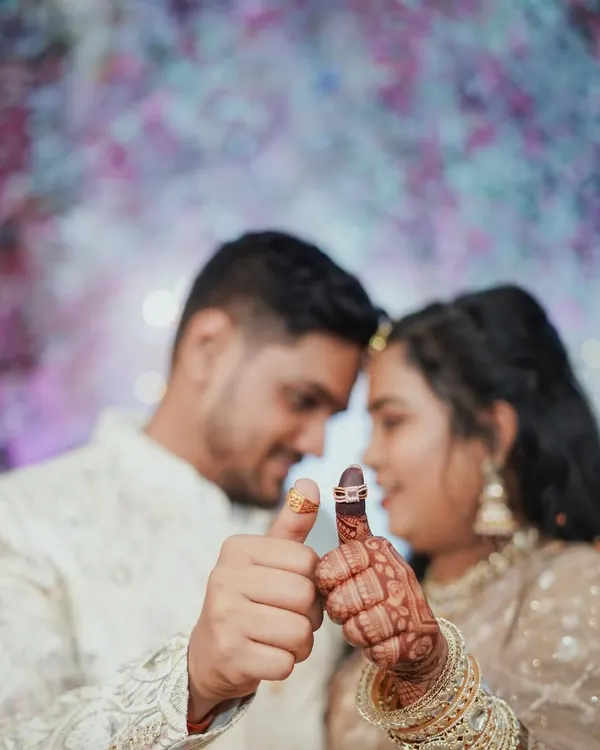 A creative engagement ring shot where the couple shows off their new rings on their thumbs. The focus is on the rings and their hands, with their happy faces blurred softly in the background.