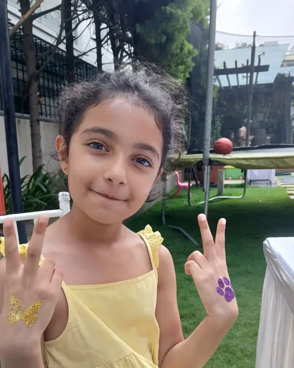Double the fun with two glitter tattoos. This happy guest is showing off a golden butterfly on one hand and a purple paw print on the other, ready for a fun-filled party.