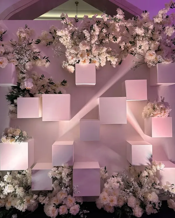 An all-white photo backdrop for a chic reception. The geometric cubes and delicate white blossoms create a modern, artistic, and utterly elegant setting. 🤍