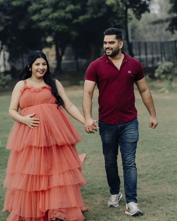 A happy couple during their maternity shoot. The mom-to-be looks radiant in our tiered coral gown, holding hands with her partner.